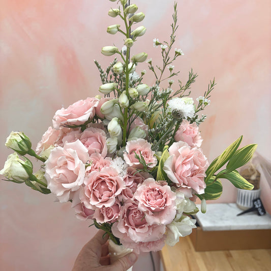 Bouquet of pink and white flowers held by a hand against a blurred indoor background
