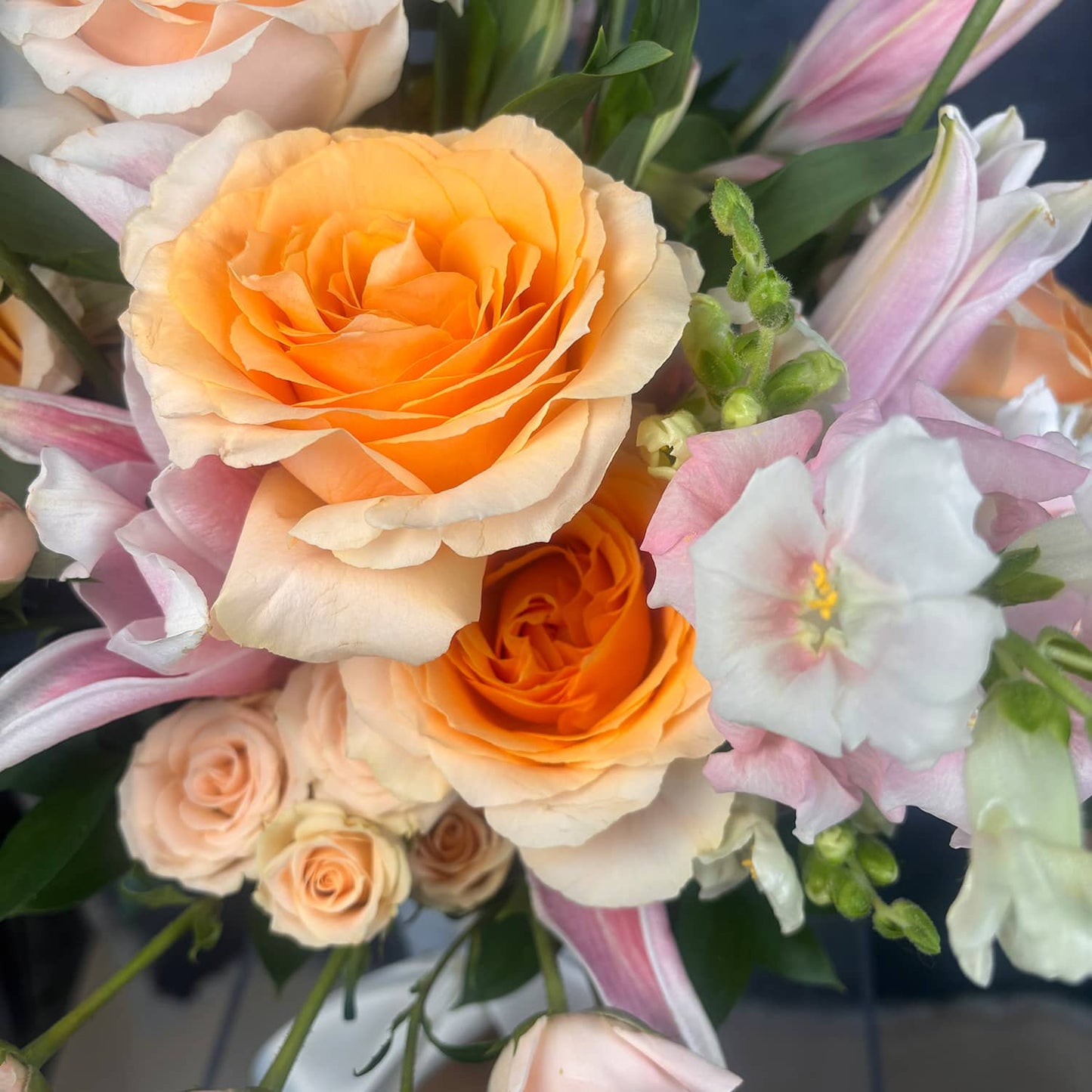 Bouquet of orange, pink, and white flowers with green leaves.