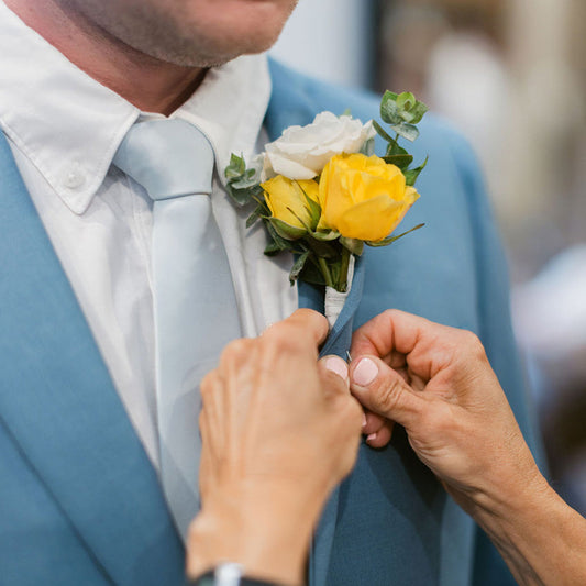 Person adjusting a yellow and white flower boutonniere on a blue suit jacket.