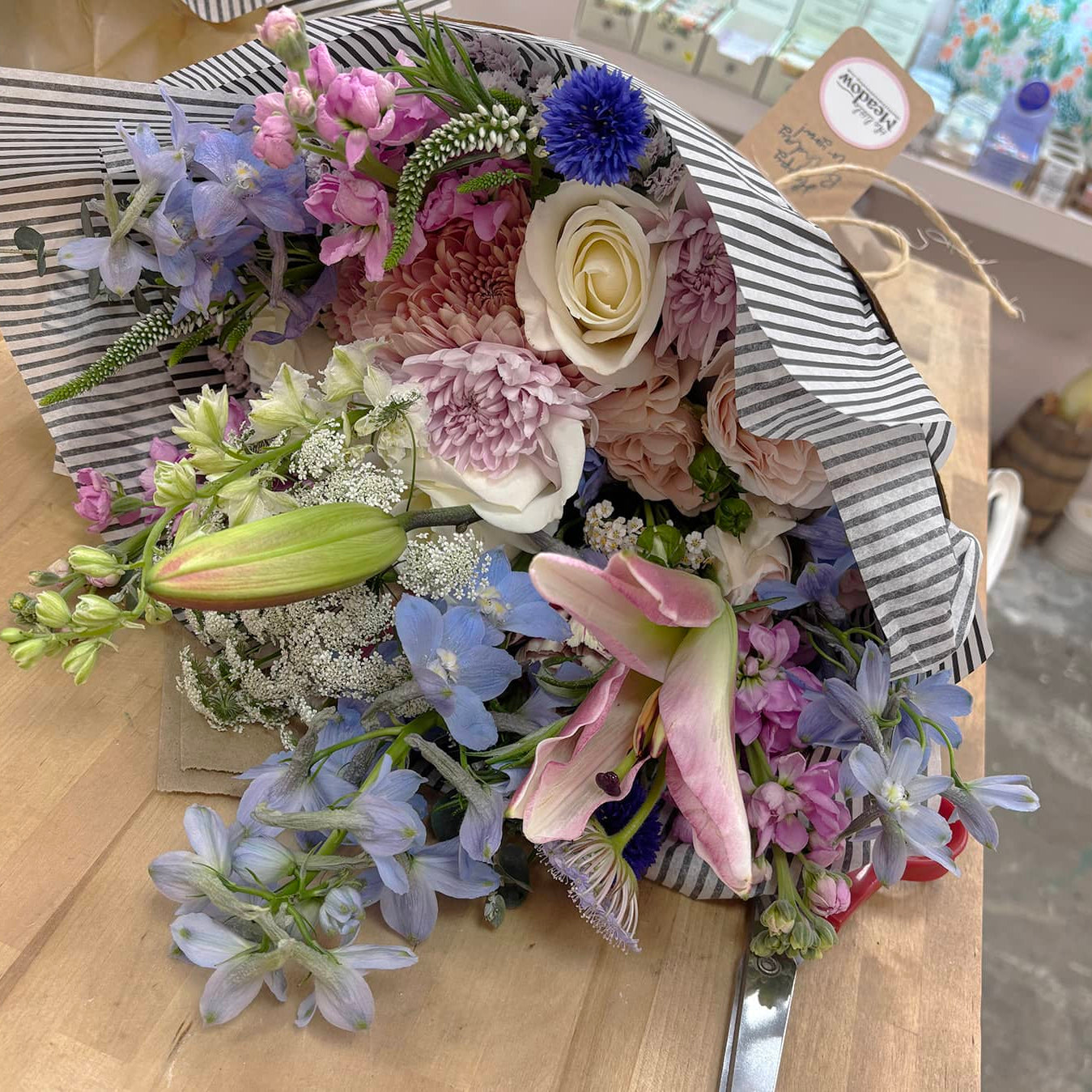 A bouquet of flowers including roses in shades of pink, yellow, and white, arranged in a wrapped paper design.
