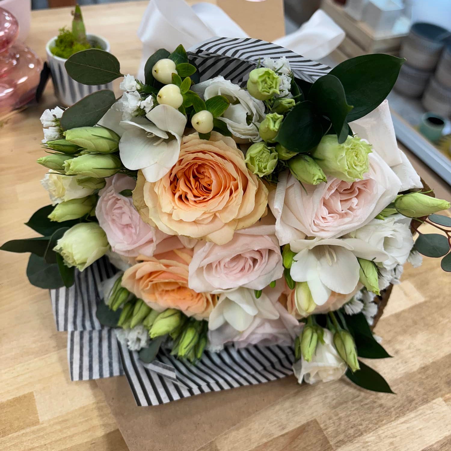 A bouquet of flowers including roses in shades of pink, yellow, and white, arranged in a wrapped paper design.