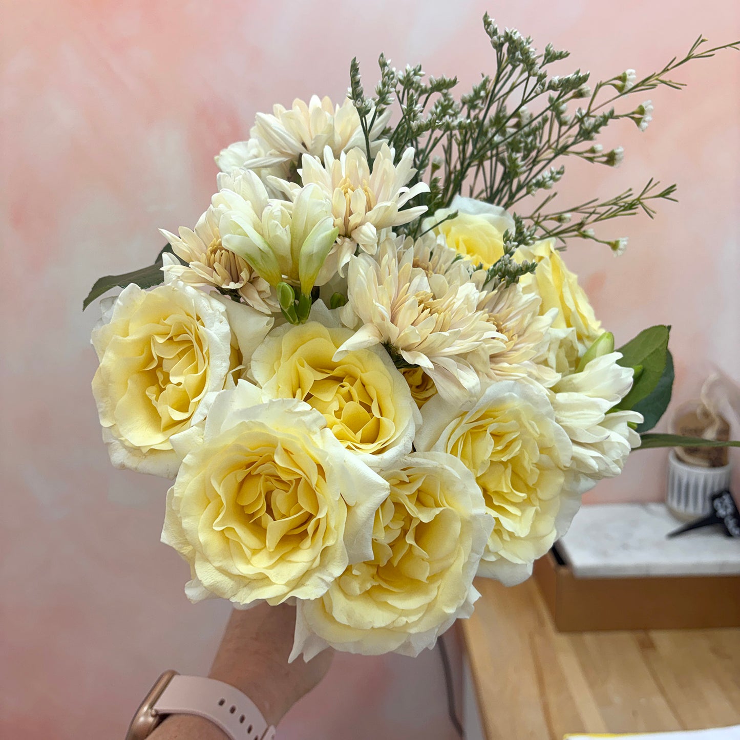 Bouquet of white and yellow flowers held by a person with a blurred indoor background