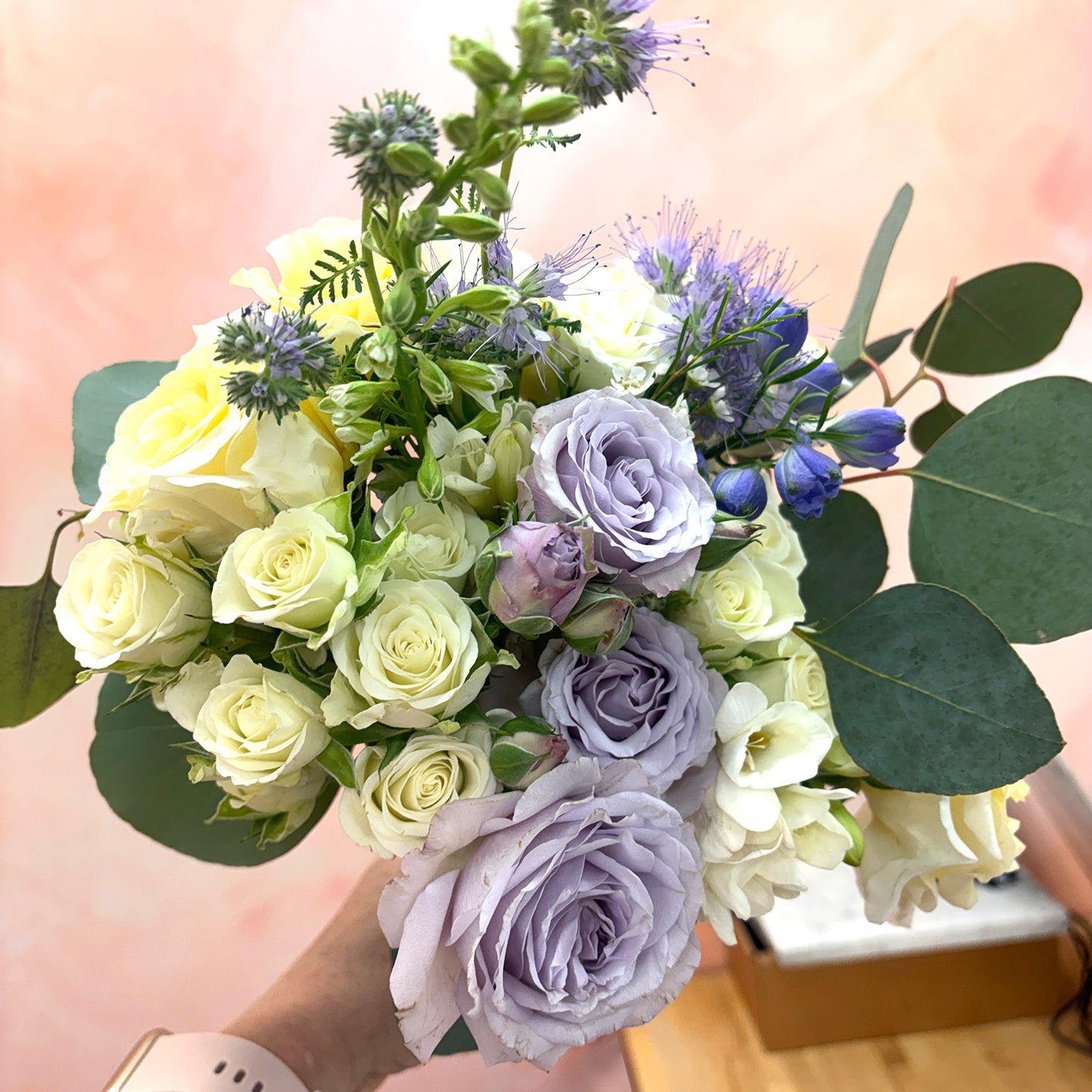 Bouquet of flowers with greenery held by a person against a blurred background